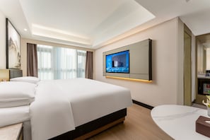 A modern hotel room with a large bed, a flat-screen TV mounted on the wall, and a small round table with a vase.