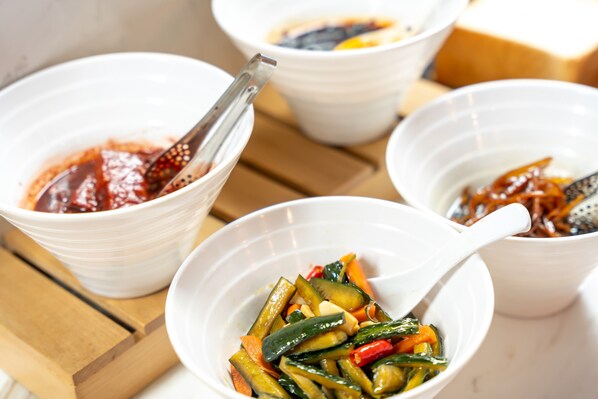 Four white bowls with various vegetables and sauces, placed on a wooden table.