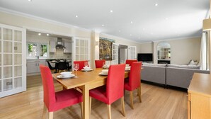 A modern dining area with a wooden table and red chairs, a grey sofa, and a TV in the background. - Ascot Spacious 4 Bedroom Home with Driveway (Ascot)