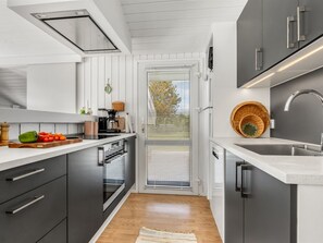 A modern kitchen with a built-in oven, a sink, and a window with blinds.