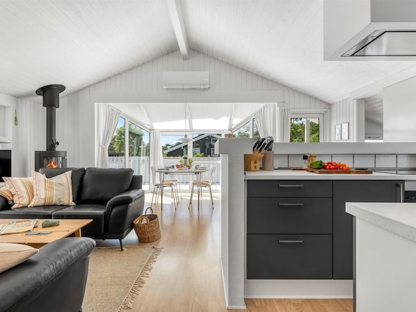 A modern kitchen with a central island, a dining area with a table and chairs, a black leather sofa, and a fireplace.