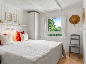 Un dormitorio con una cama, una ventana con cortinas, una silla y una obra de arte colgada en la pared.