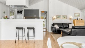A modern kitchen with a central island, two bar stools, a black leather sofa, and a dining area with a white table and chairs. - "Henri" - 1.2km from the sea by Interhome (Hjørring)