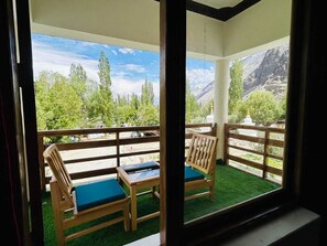 A balcony with two wooden chairs and a table, a wooden railing, and a view of a mountainous landscape.