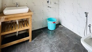 Une salle de bain avec un meuble-lavabo en bois, un évier, un miroir, un seau bleu, un espace douche et des toilettes.