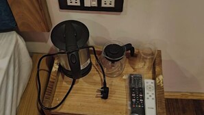 Une table de chevet en bois avec une bouilloire, un verre et une télécommande.