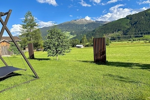 Un campo cubierto de césped con un columpio, árboles y una montaña al fondo.