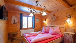 Un dormitorio de cabaña de madera con cama, mesita de noche, luces empotradas en la pared y lámpara en el techo.