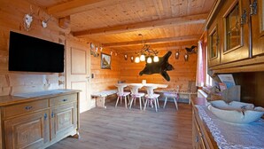 Interior de una cabaña de madera con comedor, televisor montado en la pared y adornos de cuernos.