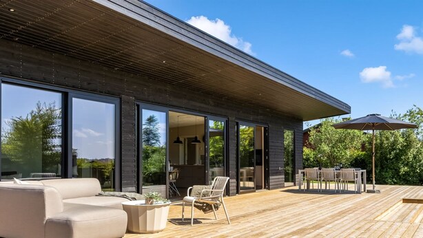 A modern outdoor deck with a wooden floor, a beige sofa, and a dining area with chairs and an umbrella. - "Edvia" - 200m to the fjord by Interhome (Holbæk)