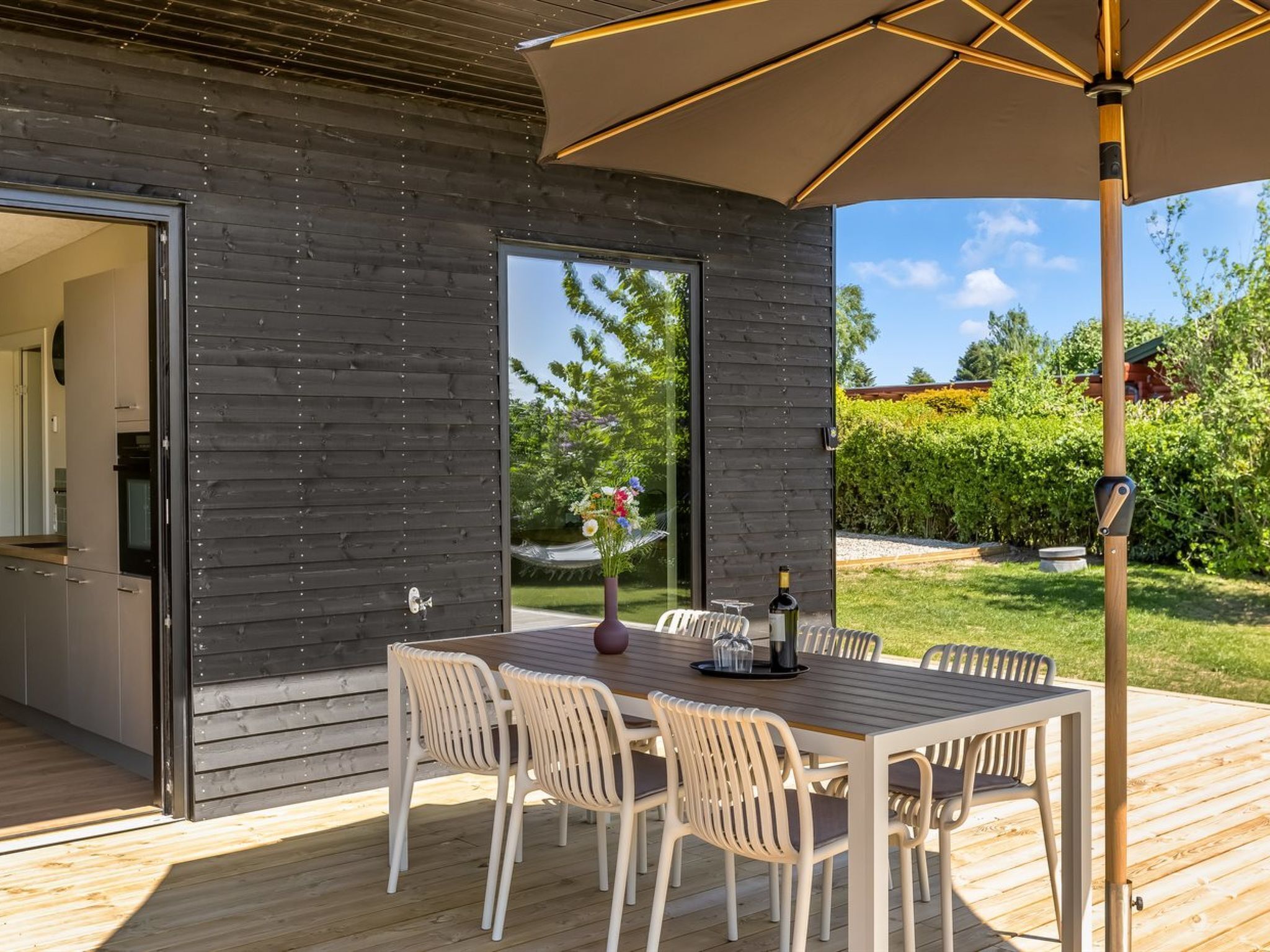 An outdoor dining area with a wooden table and chairs, a large umbrella, and a bottle of wine.