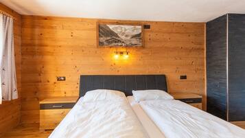 A wooden room with two beds, a nightstand, a wall-mounted light, and a picture of a mountain scene.
