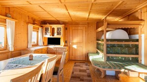A wooden cabin interior with a dining table, chairs, a bench, a small kitchen area, and a bed with a green patterned headboard. - Chalet in Mayrhofen near Ski Slopes (Hippach im Zillertal)