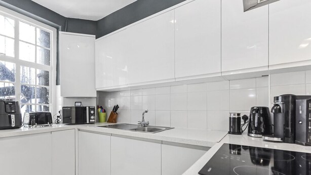 Une cuisine moderne avec des meubles blancs, un plan de travail noir et une fenêtre donnant sur un paysage enneigé.