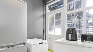 Une cuisine moderne avec un réfrigérateur blanc, un lave-linge et une machine à café posés sur le plan de travail.