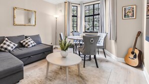 Un salon avec un canapé gris, une table ronde blanche et un coin repas avec des chaises.