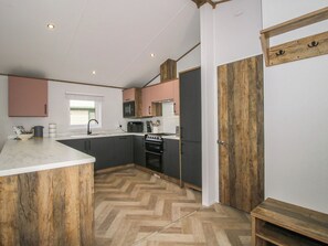 A compact kitchen with a herringbone floor, a built-in oven, and a microwave. - Peony (Leominster)