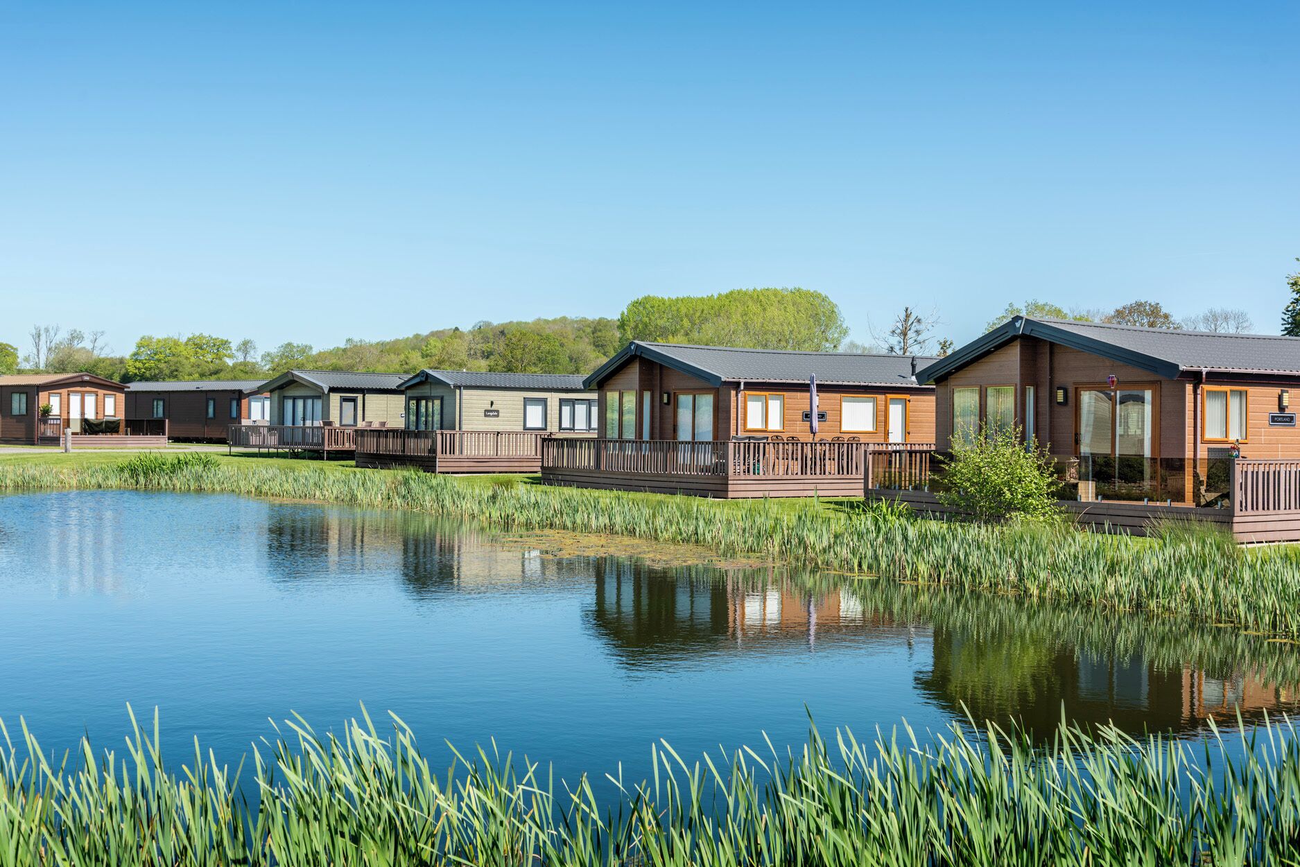 A row of cabins with wooden decks, a calm lake, and surrounding greenery.