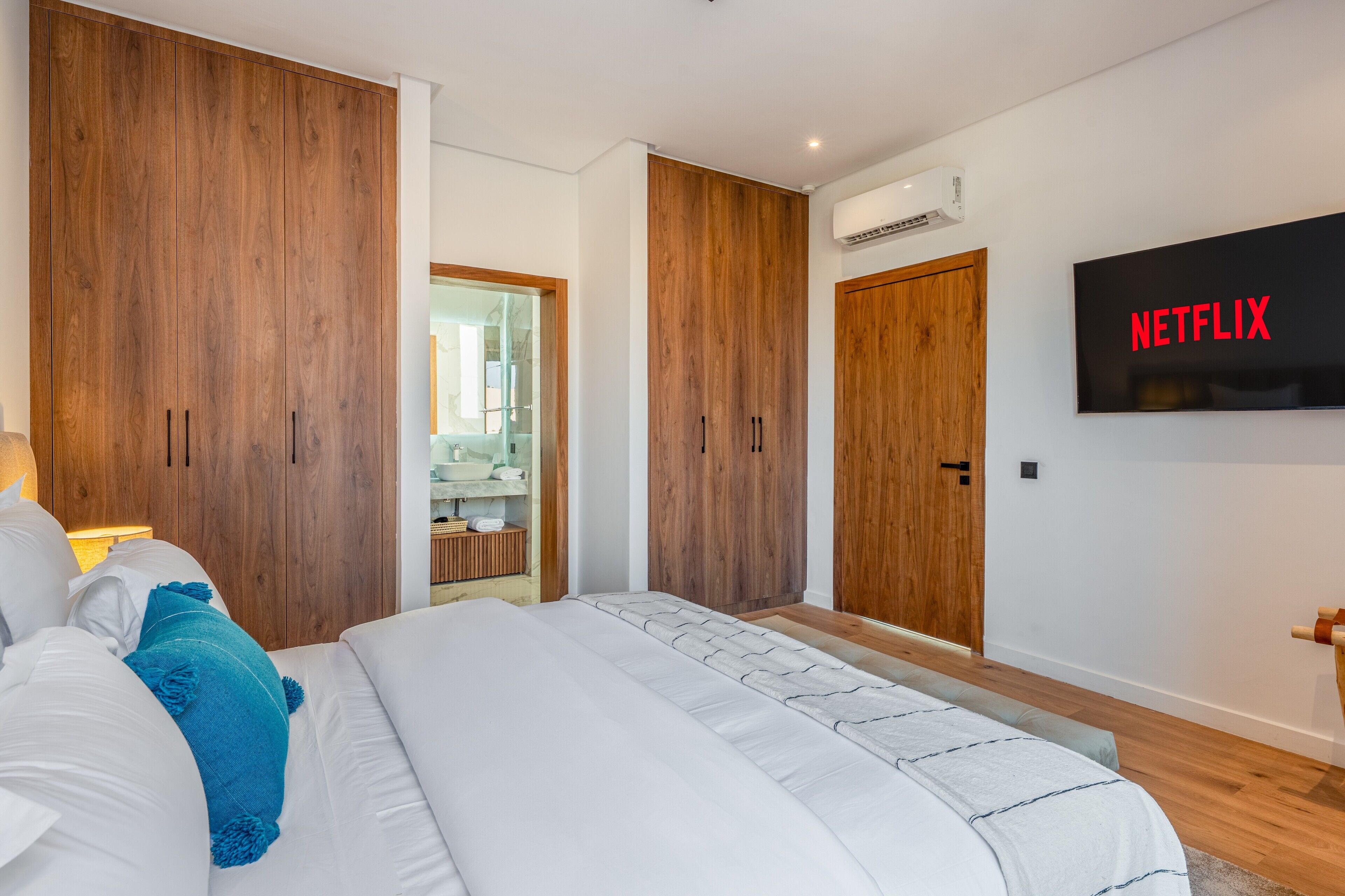 A bedroom with a bed, wooden wardrobes, a TV mounted on the wall, and a mirror.
