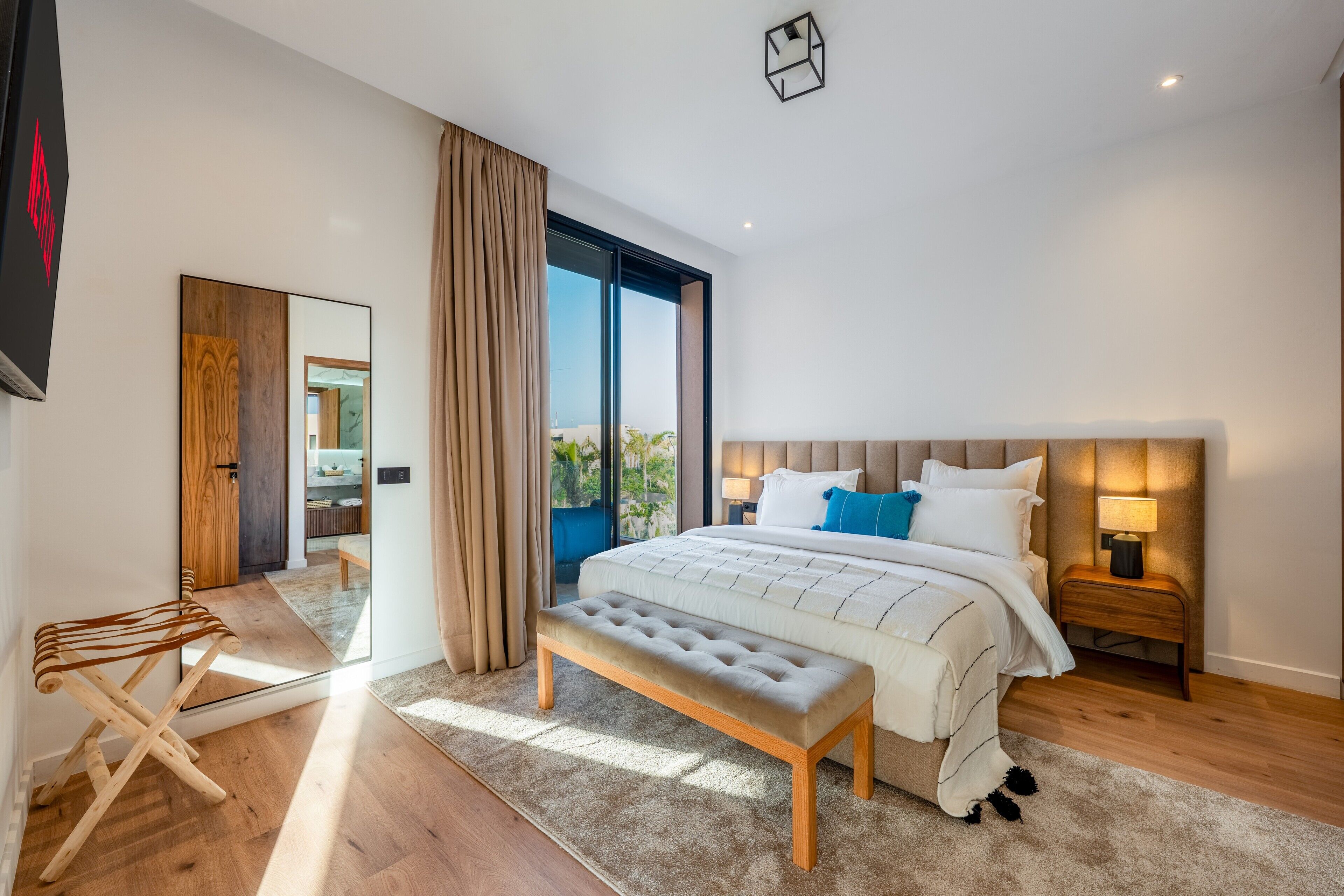 Camera da letto moderna con un letto grande, una panca, un comodino, uno specchio e vista sull'esterno.