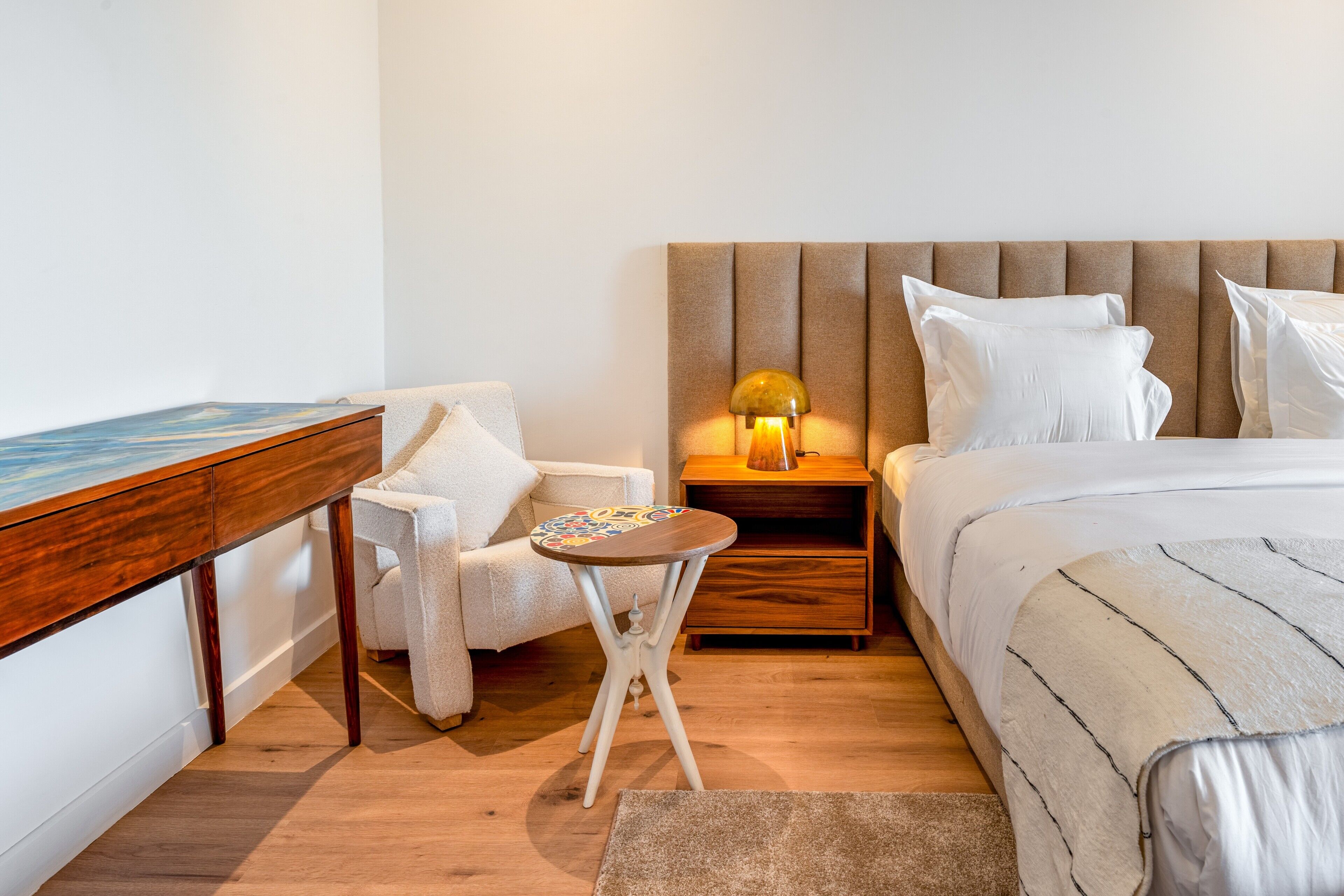A bedroom with a bed, a nightstand, a chair, a small table, and a painting on the wall.