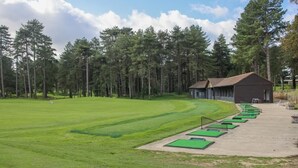 Un campo de golf con club house, calles amplias de color verde y una zona boscosa.