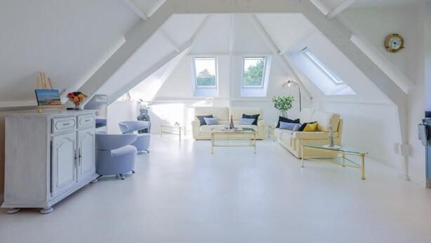 Un loft amplio con techos altos, tragaluces, una decoración en tonos blancos y una sala de estar moderna con sofás y una mesa de centro.