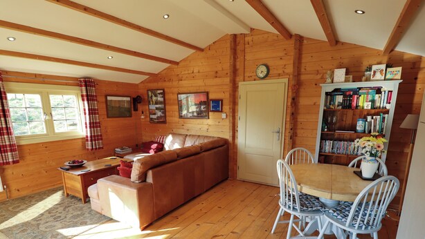 Ein gemütliches Blockhaus-Interieur mit einer Couch, einem Esstisch, Stühlen, einem Bücherregal und einer Tür.