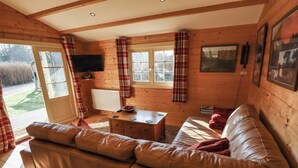 Ein gemütliches Blockhaus-Interieur mit Ledersofa, Holzesstisch und karierten Vorhängen.