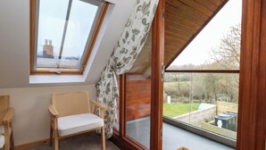 Ein Zimmer mit schrägen Wänden, einem Fenster mit Blick ins Freie, einem hölzernen Stuhl und einem Holztisch.