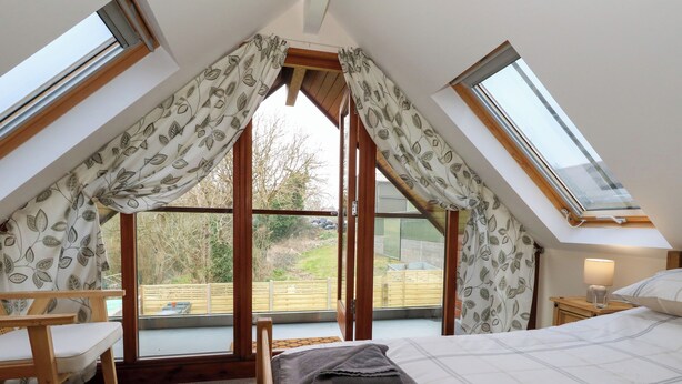 Ein Schlafzimmer mit schrägverdeckter Decke, einem Bett, einem Sessel und einem Nachttisch mit Lampe.