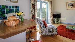 Una sala de estar con una mesa de madera, una silla, un televisor y una ventana con cortinas.