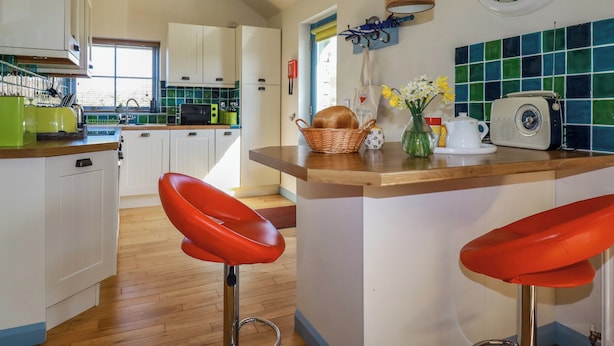 Una cocina con armarios blancos, encimera de madera y un taburete rojo.