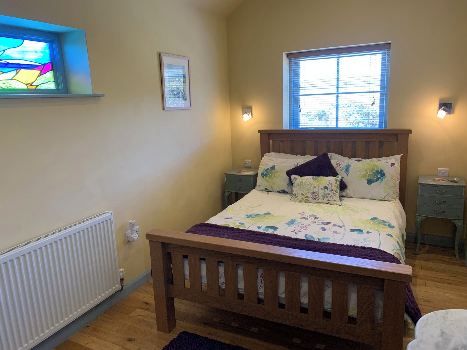 Une chambre à coucher avec un lit en bois, une fenêtre, un radiateur et une petite table de chevet.