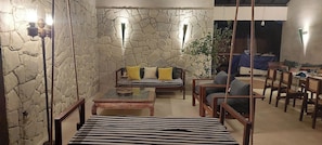 A dining area with a stone wall, hanging lights, a sofa with cushions, and wooden chairs.