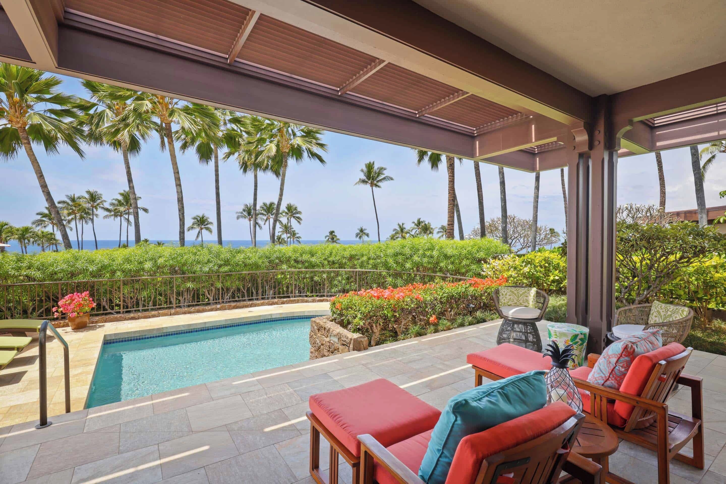 A poolside area with lounge chairs and a view of the ocean and palm trees.