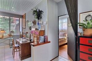 A well-lit room with a desk, chair, and a bed. There are books, a plant, and a framed picture on the desk. - Fare Nahina (Papeete)