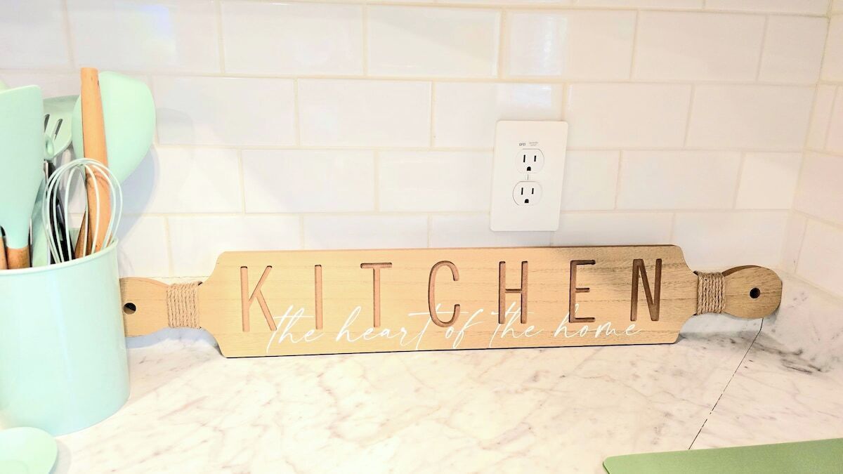 A kitchen sign with the word "KITCHEN" and the phrase "the heart of the home" on a marble countertop.