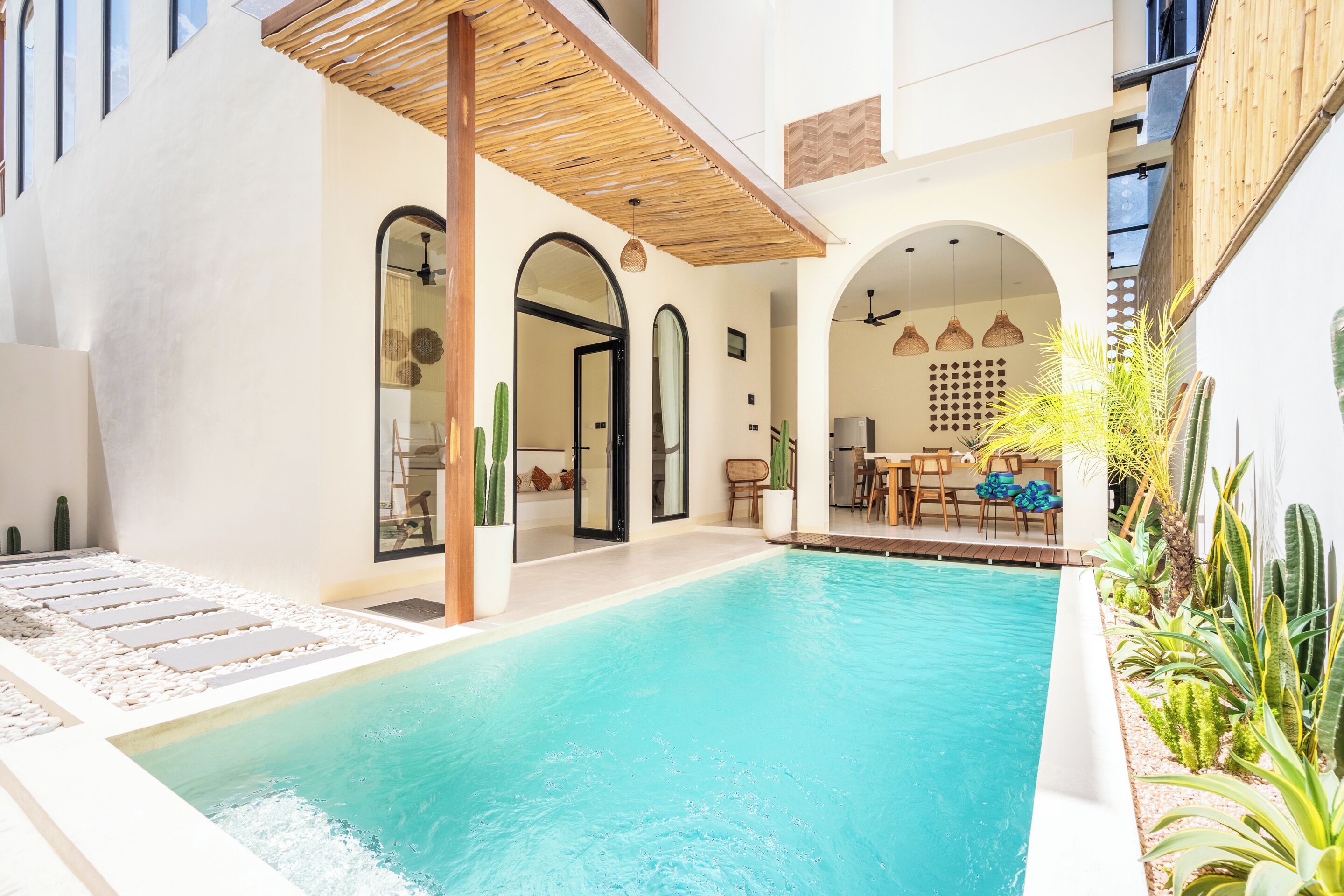 Una piscina con interior blanco, rodeada por un patio con asientos y plantas.
