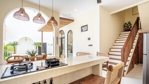 Una cocina moderna con una isla central, lámparas colgantes y una escalera de madera.