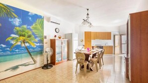 A modern kitchen with wooden cabinets, a dining area with a table and chairs, and a large tropical mural on the wall. - Terrace House by the Sea, Ac, Torre Lapillo (Torre Lapillo)