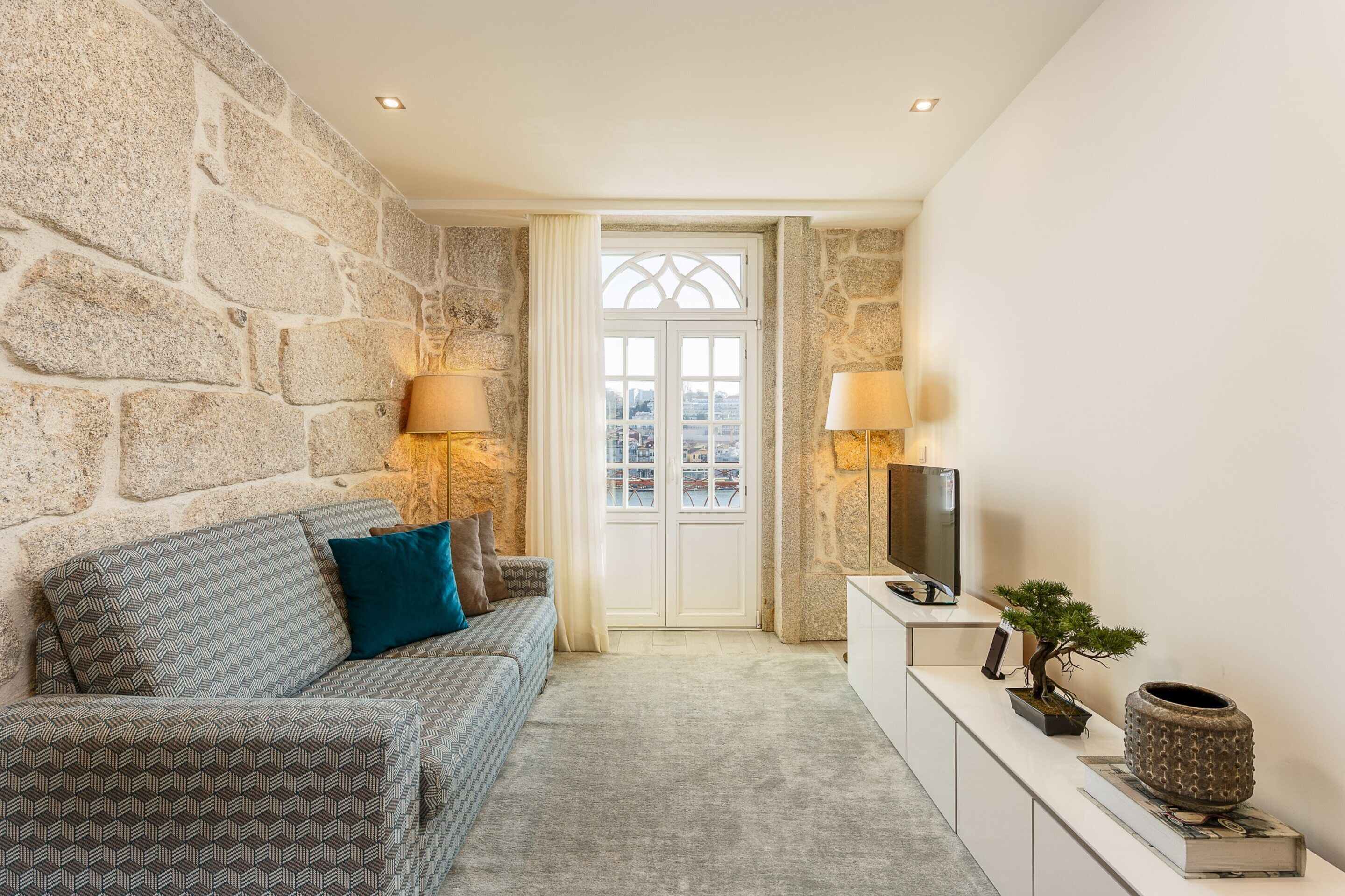 A living room with a stone wall, a sofa with patterned cushions, a television, and a potted plant.