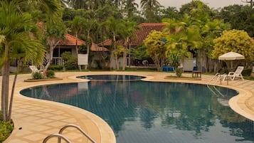 A swimming pool with a tiled edge, surrounded by palm trees and a building with a red roof.