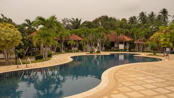A swimming pool with a curved design, surrounded by palm trees and buildings with red-tiled roofs.