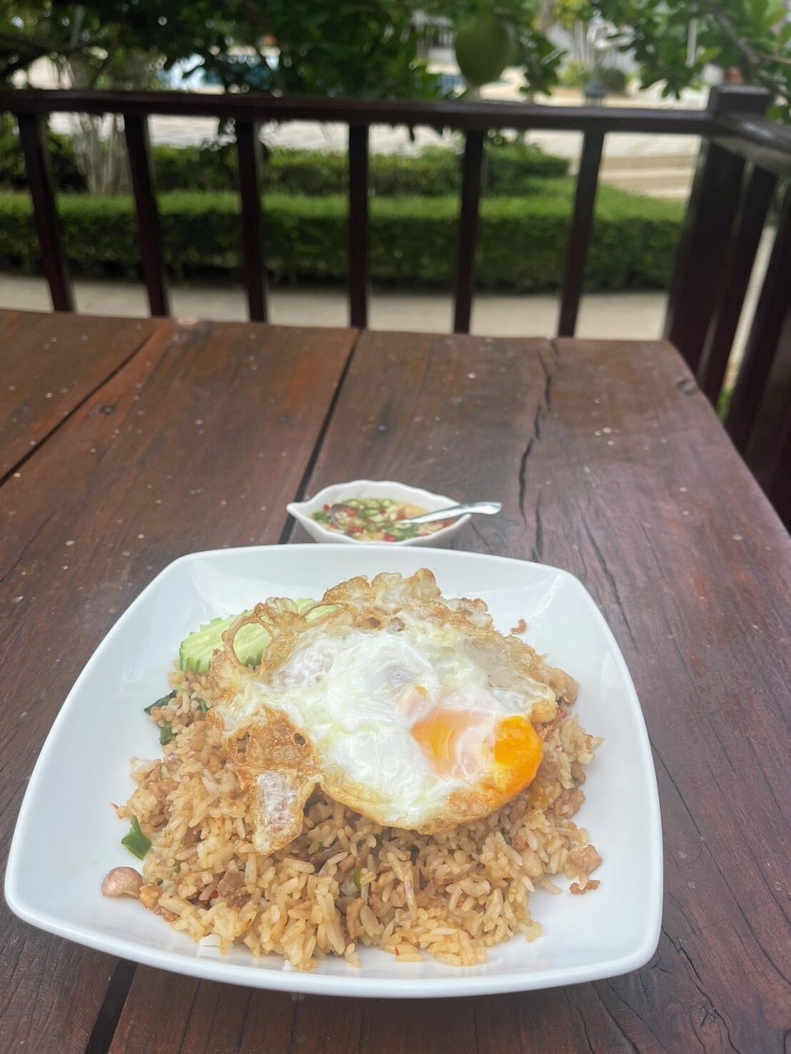 A square white plate of fried rice with an egg on a wooden table.