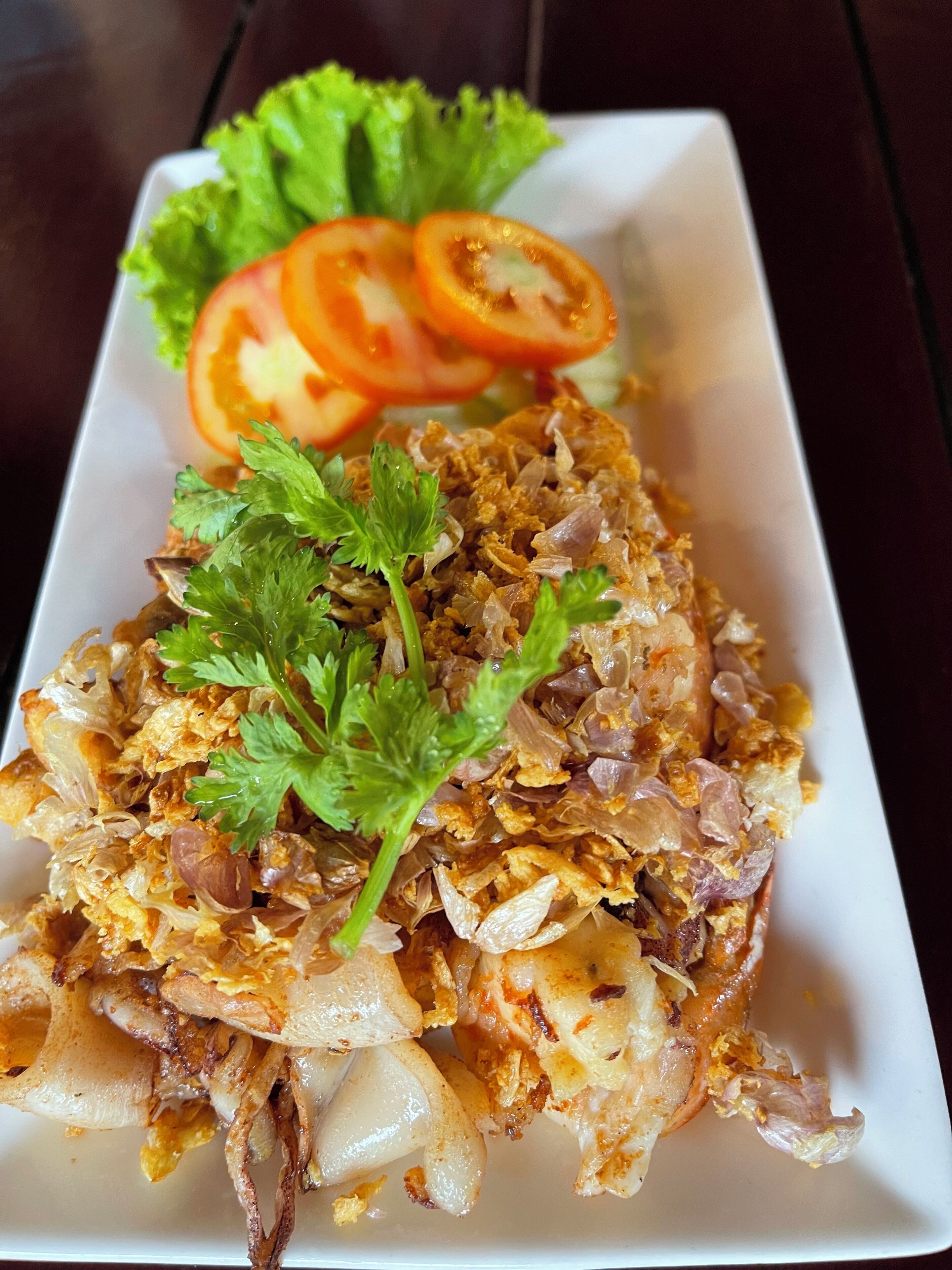A plate of fried fish garnished with onions and parsley, accompanied by a side of sliced tomatoes and lettuce.