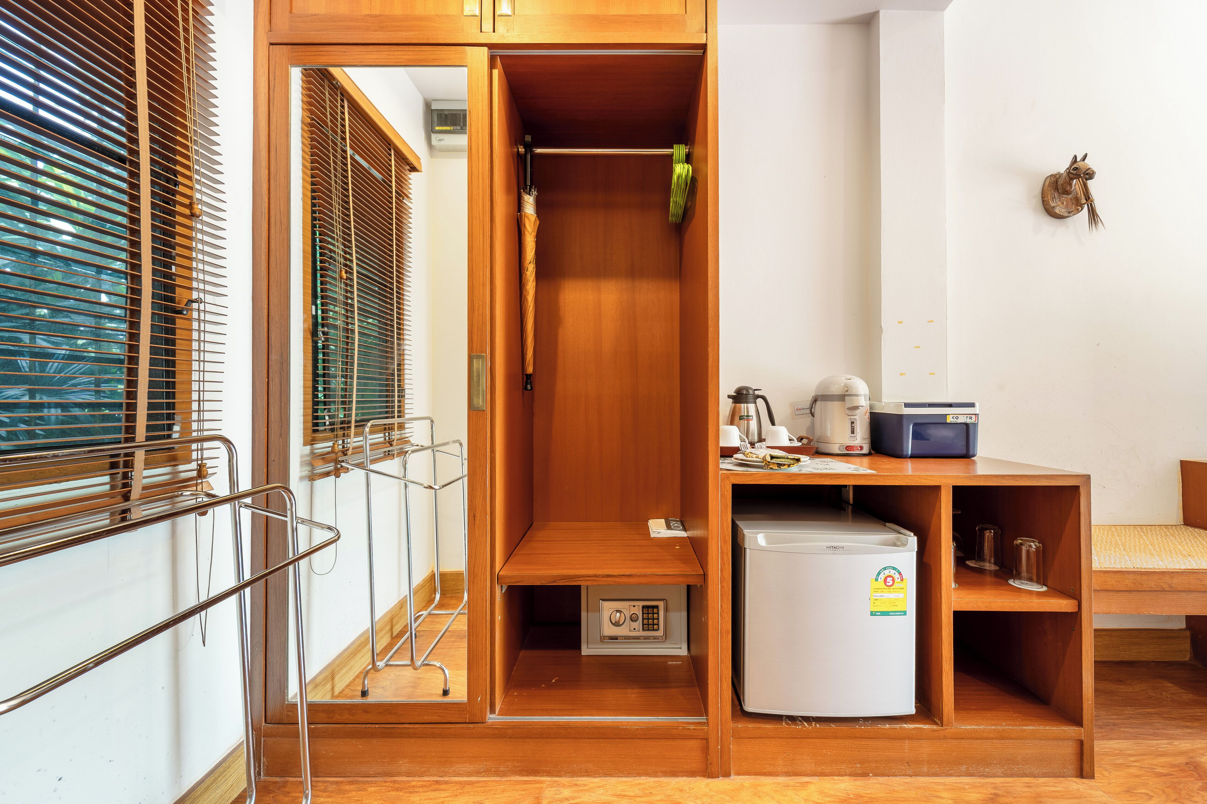 Une chambre de taille modeste, dotée d’une armoire en bois, d’une petite table avec une bouilloire et d’un réfrigérateur.