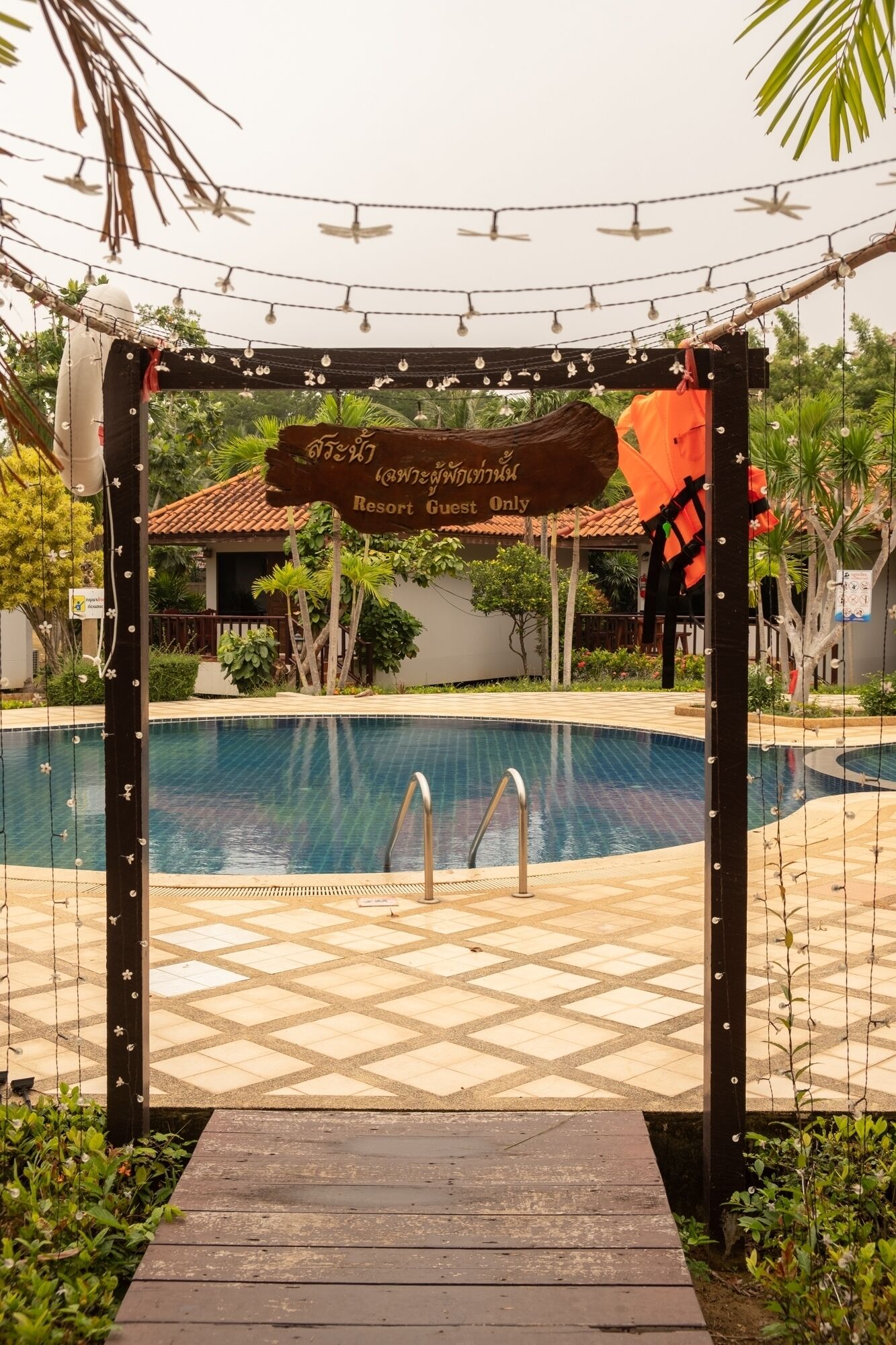 Zona de piscina en un resort con un arco de madera con el letrero 'Resort Guest Only' y un cartel en un idioma extranjero.