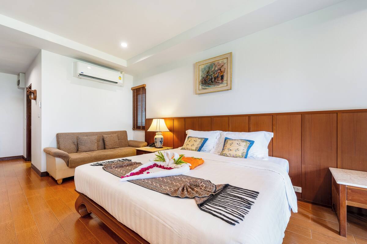 A hotel room with a bed, a sofa, a lamp, and a painting on the wall.