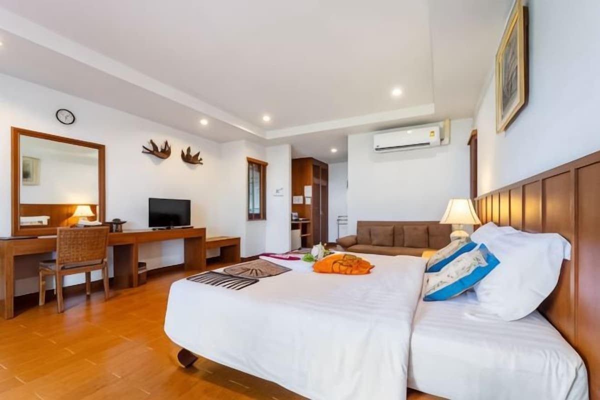 A hotel room with a large bed, a desk, a chair, a television, and a wardrobe.